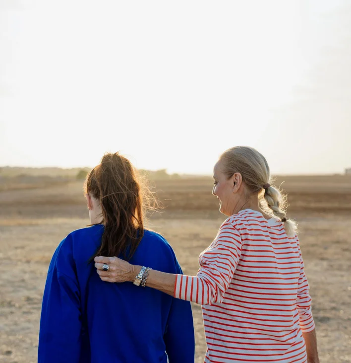 Mother and daughter on beach walking away. Mother's arm on daughters shoulder.