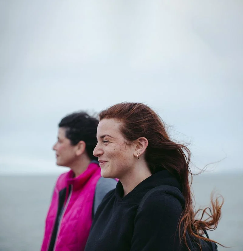 Two women standing on beach on grey windy day