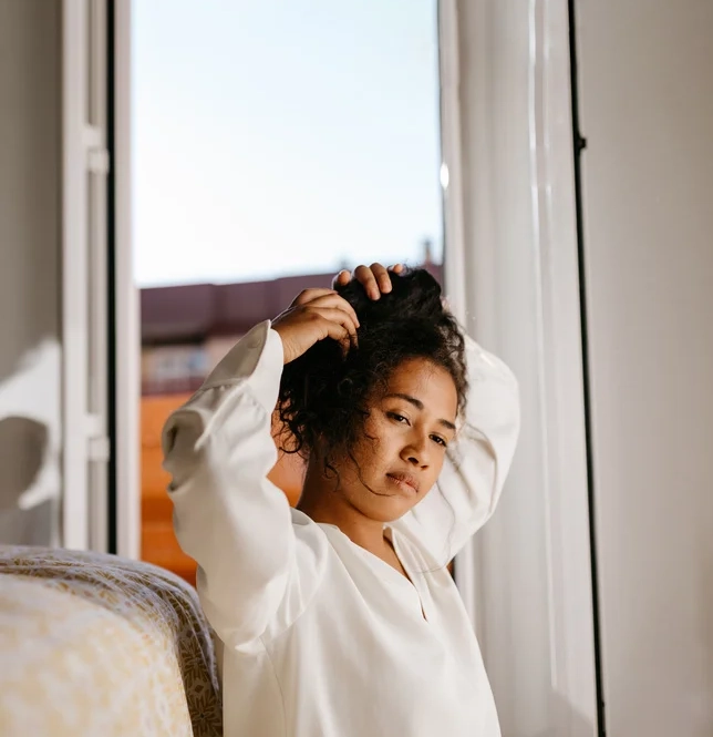 Woman sitting at foot of bed tying up her hair